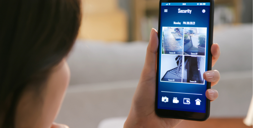 mulher de costas olhando para tela do celular onde tem as câmeras da casa